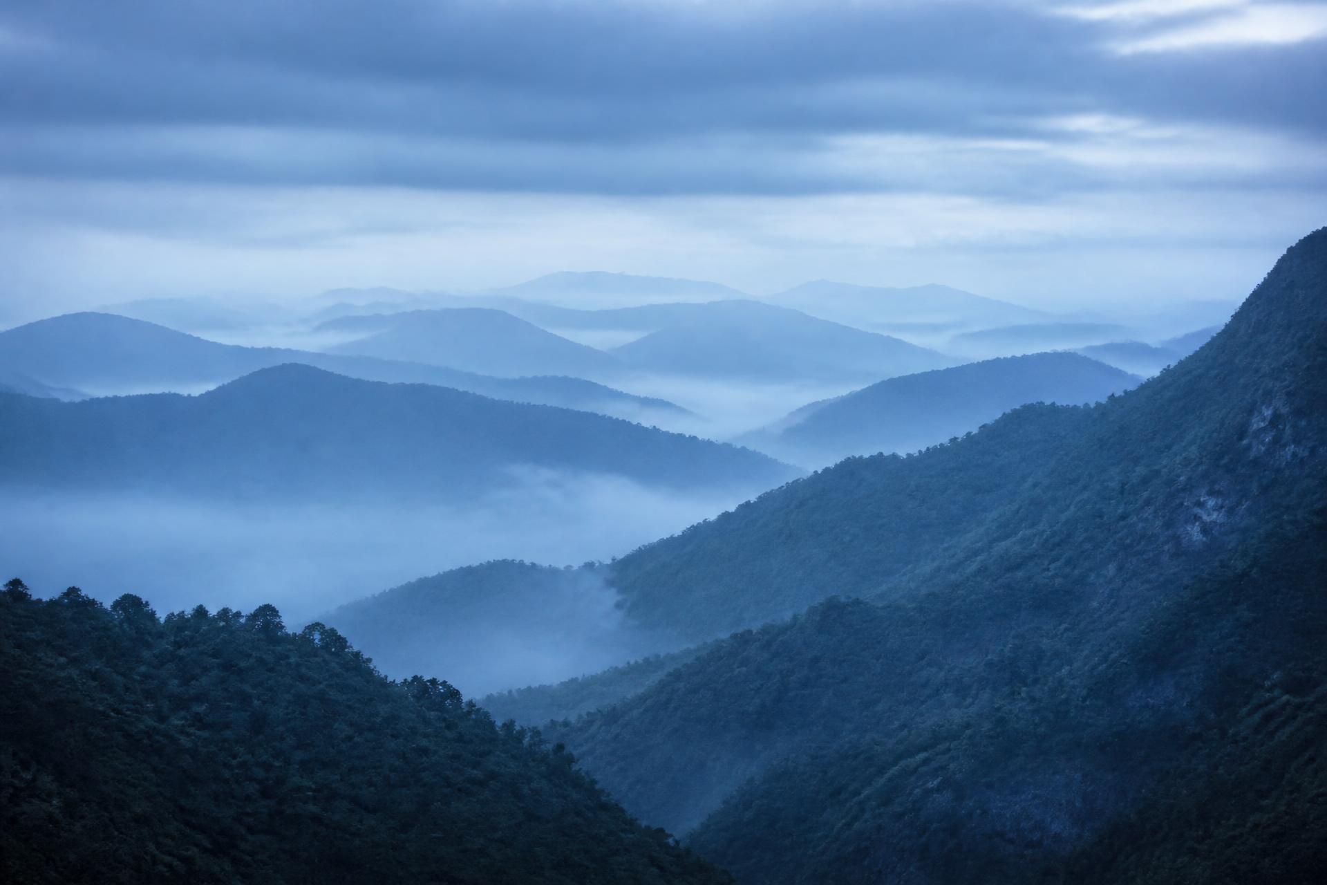 Misty layered mountain ridges fading into fog, graded cool blue